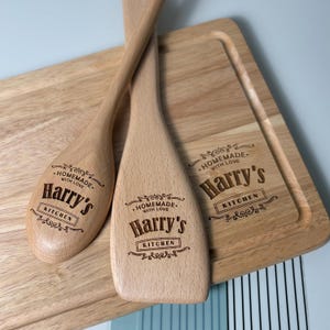 May include: Two light-colored wooden kitchen spoons and a rectangular wooden cutting board. Each item is laser-engraved with the text "HOMEMADE WITH LOVE", "Harry's", and "KITCHEN" surrounded by decorative scrollwork flourishes.