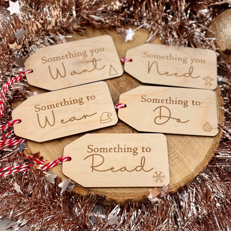 May include: Five wooden gift tags with red and white twine. The tags are labelled "Something you Want", "Something you Need", "Something to Wear", "Something to Do", and "Something to Read".