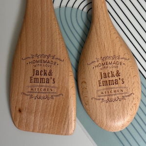 May include: Two light brown wooden kitchen utensils, a flat spatula and a rounded spoon, each featuring a laser-engraved design that reads "HOMEMADE WITH LOVE Jack & Emma's KITCHEN" surrounded by decorative flourishes and scrollwork.