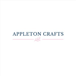 May include: A logo featuring the text APPLETON CRAFTS in dark blue capital letters. Below the text is a thin horizontal pink line interrupted in the center by a small, delicate pink line drawing of a leafy branch with three leaves.