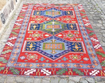 May include: A rectangular area rug featuring a vibrant red background with three large blue diamond-shaped medallions. The design includes geometric patterns in green, orange, and white, with a wide border containing repeating motifs.