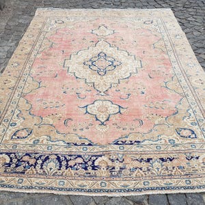 May include: A rectangular area rug featuring a central medallion in cream and blue on a soft pink field. The rug is decorated with intricate floral and vine motifs in shades of blue and beige, framed by a wide, dark blue border with floral patterns.