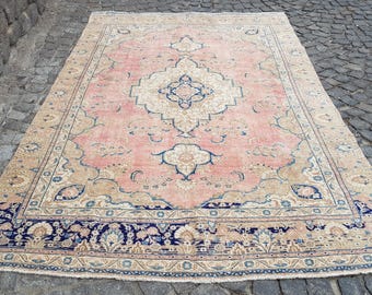 May include: A rectangular area rug featuring a central medallion in cream and blue on a soft pink field. The rug is decorated with intricate floral and vine motifs in shades of blue and beige, framed by a wide, dark blue border with floral patterns.