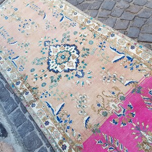 May include: A rectangular area rug featuring a faded peach background with a central dark blue and white floral medallion. The design includes intricate botanical patterns in shades of blue, green, and cream, with a vibrant hot pink section at one end.
