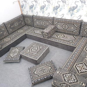 May include: A gray sectional sofa with matching ottomans and throw pillows. The sofa and ottomans have a geometric pattern in shades of gray, black, and white. The sofa is arranged in an L-shape, with several cushions and pillows.