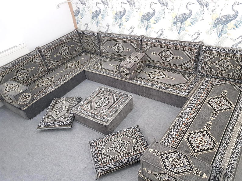 May include: A gray sectional sofa with matching ottomans and throw pillows. The sofa and ottomans have a geometric pattern in shades of gray, black, and white. The sofa is arranged in an L-shape, with several cushions and pillows.
