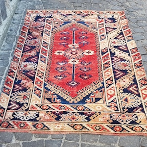 May include: A rectangular area rug featuring a vibrant red central field with a dark blue diamond-shaped medallion and intricate geometric floral motifs. The border displays repeating patterns in shades of cream, dark blue, and red throughout.
