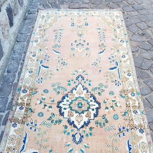 May include: A rectangular runner rug featuring a soft peach background with a central dark blue and white medallion. The rug is decorated with intricate floral patterns in shades of teal, light blue, and beige, framed by a detailed border.