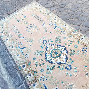 May include: A rectangular area rug featuring a soft peach background with a central dark blue and white floral medallion. The rug is decorated with intricate botanical patterns in shades of blue, teal, and beige, framed by a detailed border.