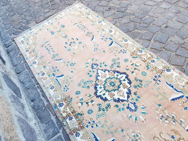 May include: A rectangular area rug featuring a soft peach background with a central dark blue and white floral medallion. The rug is decorated with intricate botanical patterns in shades of blue, teal, and beige, framed by a detailed border.