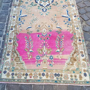 May include: A rectangular area rug featuring a central field of vibrant hot pink transitioning into a soft peach tone. The rug is decorated with intricate floral and botanical motifs in shades of blue, cream, and brown, framed by a detailed border.