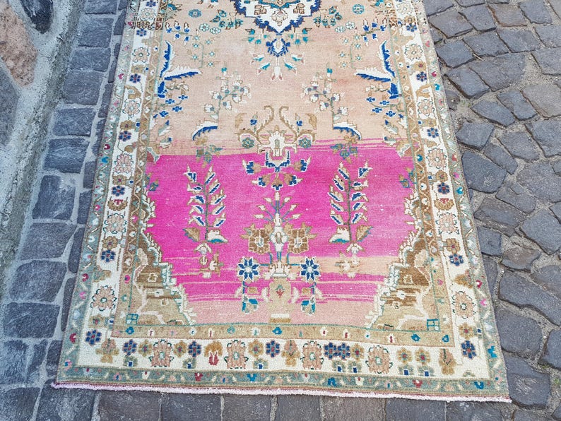 May include: A rectangular area rug featuring a central field of vibrant hot pink transitioning into a soft peach tone. The rug is decorated with intricate floral and botanical motifs in shades of blue, cream, and brown, framed by a detailed border.