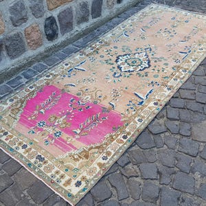 May include: A rectangular runner rug featuring a large section of vibrant hot pink at one end, transitioning into a soft peach field. The rug is decorated with intricate floral motifs, scrolling vines, and a central medallion in blue and cream.