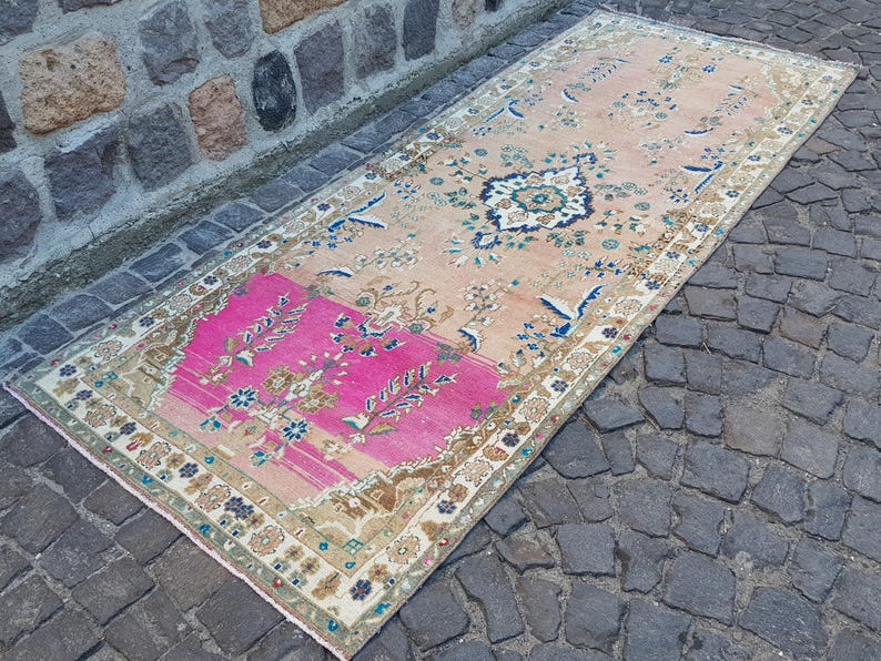 May include: A rectangular runner rug featuring a large section of vibrant hot pink at one end, transitioning into a soft peach field. The rug is decorated with intricate floral motifs, scrolling vines, and a central medallion in blue and cream.