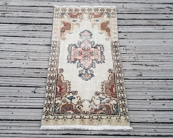 Puede incluir: Una alfombra rectangular con un campo de color crema y un medallón central en tonos rosa, azul y marrón oscuro. La alfombra presenta un borde decorativo con motivos florales y flecos blancos cortos en ambos extremos del tejido.