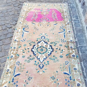 May include: A rectangular runner rug featuring a central dark blue and white geometric medallion on a light peach background. The rug includes a vibrant pink section at one end, decorated with intricate floral patterns in blue, green, and white.