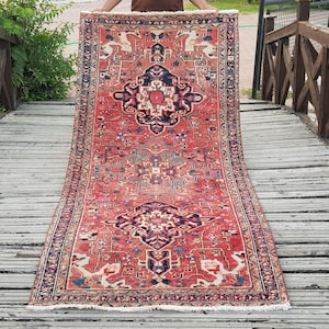 May include: A rectangular area rug featuring a vibrant red background with intricate navy blue, cream, and light blue geometric patterns. The design includes central medallion motifs and a detailed border, finished with short white fringe at both ends.