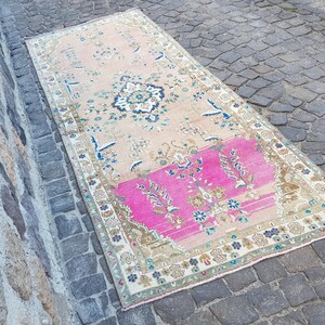 May include: A rectangular area rug featuring a faded peach background with a prominent bright pink section at one end. The rug displays intricate floral and geometric patterns in shades of blue, cream, and brown, finished with a decorative border.
