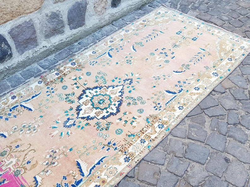 May include: A rectangular area rug featuring a light peach background with a central medallion in navy blue, white, and teal. The rug is decorated with intricate floral and vine patterns in shades of blue, green, and tan, finished with a patterned border.