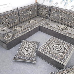 May include: A gray sectional sofa with matching ottomans and throw pillows. The sofa and ottomans have a geometric pattern in shades of gray, black, and white. The pillows have a similar design. The furniture is arranged in a corner configuration.