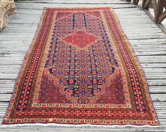 May include: A rectangular area rug featuring a deep blue central field with a repeating geometric pattern in red, yellow, and orange. The rug has a prominent red diamond-shaped medallion in the center and a wide border with floral motifs.