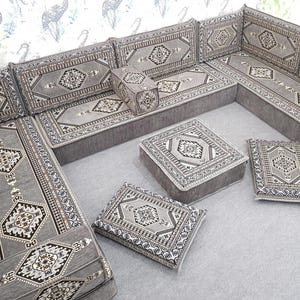 May include: A gray sectional sofa with matching square and rectangular cushions. The cushions and sofa feature a geometric pattern in shades of gray, black, and white. The sofa is arranged in an L-shape, suitable for a living room or lounge area.