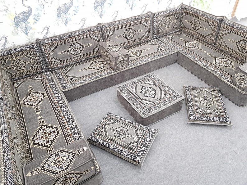 May include: A gray sectional sofa with matching square and rectangular cushions. The cushions and sofa feature a geometric pattern in shades of gray, black, and white. The sofa is arranged in an L-shape, suitable for a living room or lounge area.