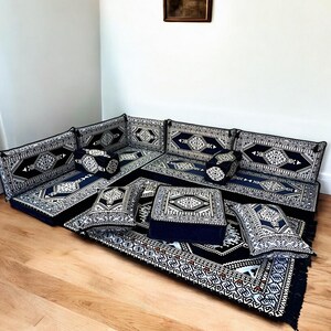 May include: A black and white patterned floor cushion set with a matching rug. The cushions are arranged in a U-shape to form a seating area. The cushions are made of a soft, plush fabric and have a comfortable, firm filling.