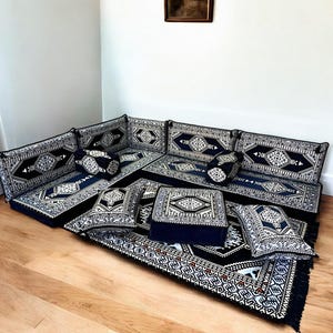 May include: A black and white patterned floor cushion set with a matching rug. The cushions are arranged in a U-shape to form a seating area. The cushions are made of a soft, plush fabric and have a traditional design.