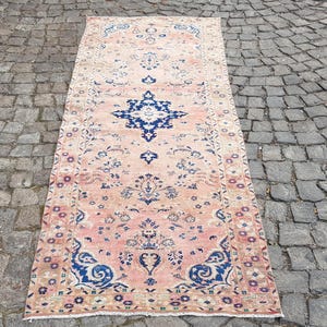 Op de afbeelding: Een rechthoekige loper met een vervaagde perzik- en lichtroze achtergrond, voorzien van complexe bloem- en geometrische patronen in donkerblauw en crème. Het ontwerp bevat een centraal medaillon en een gedetailleerde rand met symmetrische motieven.