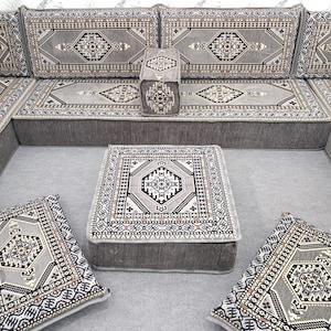 May include: A gray sectional sofa with matching cushions and a square ottoman. The cushions and ottoman feature a detailed geometric pattern in shades of gray, black, and white. The sofa is designed for a living room.