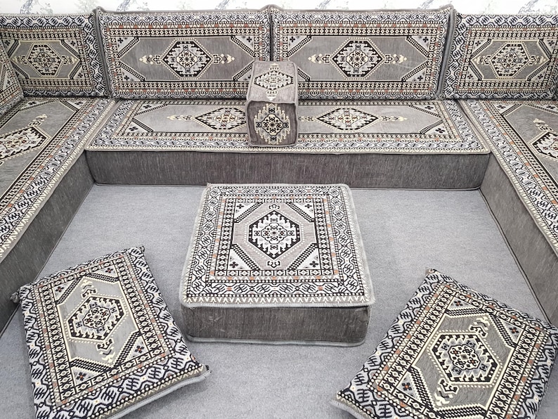 May include: A gray sectional sofa with matching cushions and a square ottoman. The cushions and ottoman feature a detailed geometric pattern in shades of gray, black, and white. The sofa is designed for a living room.