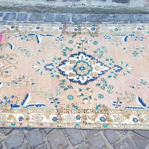 May include: A rectangular area rug featuring a light peach background with a central floral medallion in shades of blue, white, and teal. The rug includes a vibrant magenta section on the left side and a decorative border with intricate floral patterns.