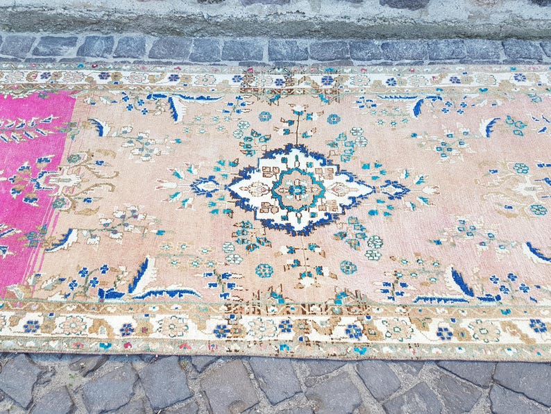 May include: A rectangular area rug featuring a light peach background with a central floral medallion in shades of blue, white, and teal. The rug includes a vibrant magenta section on the left side and a decorative border with intricate floral patterns.
