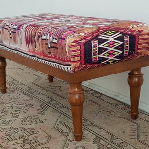 May include: A wooden bench with turned legs and a colourful patterned fabric top. The fabric features a geometric design in shades of red, pink, brown, black, and white.