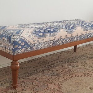 May include: A wooden bench with turned legs and a patterned fabric cushion. The cushion features a geometric design in shades of blue, pink, and white.