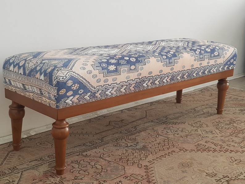 May include: A wooden bench with turned legs and a patterned fabric cushion. The cushion features a geometric design in shades of blue, pink, and white.