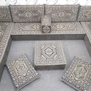 May include: A gray sectional sofa with matching cushions and a square ottoman. The cushions and ottoman feature a geometric pattern in shades of gray, black, and cream. The sofa is arranged in an L-shape, suitable for a living room.