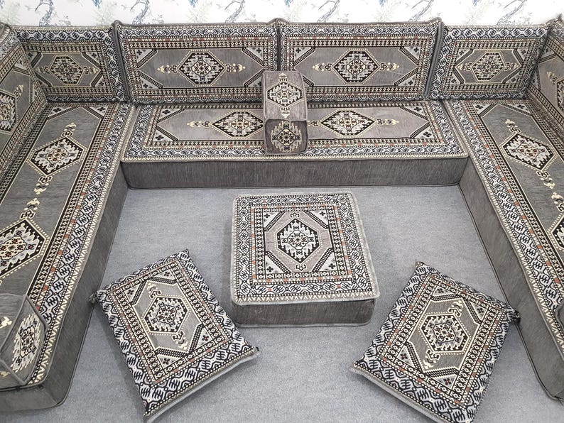 May include: A gray sectional sofa with matching cushions and a square ottoman. The cushions and ottoman feature a geometric pattern in shades of gray, black, and cream. The sofa is arranged in an L-shape, suitable for a living room.