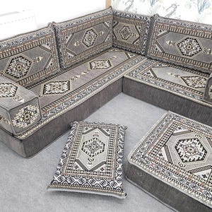 May include: A grey corner sofa with patterned cushions and a footstool. The sofa and cushions have a geometric design in grey, black, and white. The style is traditional, with a patterned aesthetic.