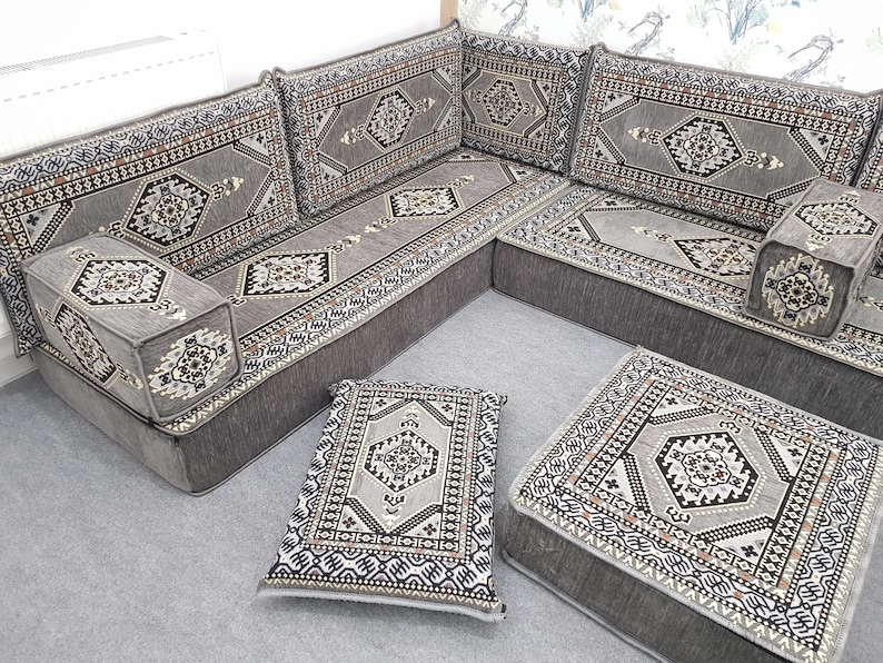 May include: A gray sectional sofa with matching cushions and a footstool. The sofa and cushions feature a geometric pattern in shades of gray, black, and white. The design has a traditional, patterned aesthetic.
