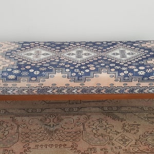 May include: A wooden bench with a blue and pink patterned cushion. The cushion has a geometric design with white accents. The bench is sitting on a rug with a similar pattern.