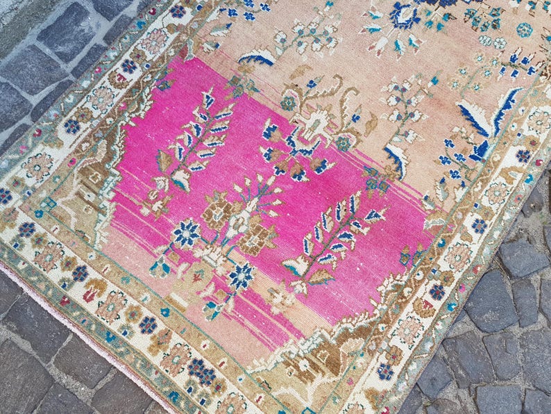 May include: A rectangular area rug featuring a vibrant hot pink central panel contrasted with soft peach sections. The rug is decorated with intricate floral and botanical motifs in shades of blue, brown, and cream, framed by a detailed patterned border.