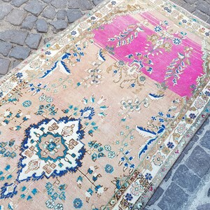 May include: A rectangular area rug featuring a central medallion and floral motifs in shades of pink, beige, blue, and white. The rug has a prominent bright pink section at one end and a detailed border pattern surrounding the entire perimeter.