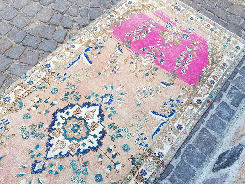 May include: A rectangular area rug featuring a central medallion and floral motifs in shades of pink, beige, blue, and white. The rug has a prominent bright pink section at one end and a detailed border pattern surrounding the entire perimeter.