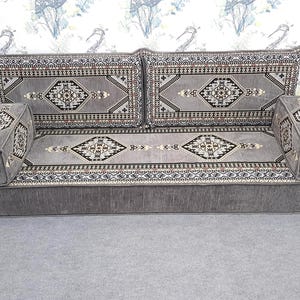 May include: A gray sofa with patterned cushions and armrests. The cushions and armrests feature a geometric design in black, white, and brown. The sofa has a low profile and a solid gray base, suitable for a living room or lounge area.