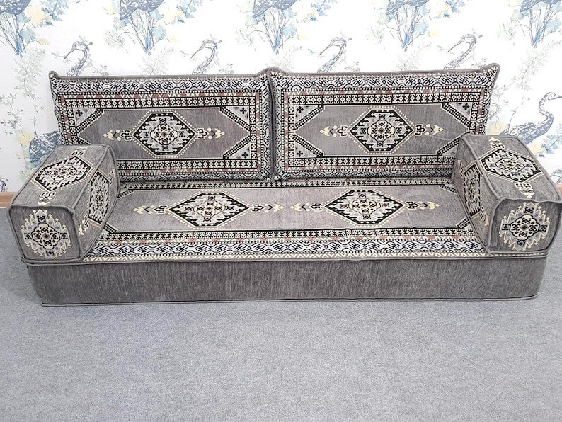 May include: A gray sofa with patterned cushions and armrests. The cushions and armrests feature a geometric design in black, white, and brown. The sofa has a low profile and a solid gray base, suitable for a living room or lounge area.