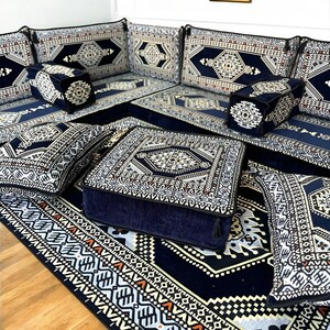 May include: A set of blue and white patterned floor cushions and a matching rug. The cushions are arranged in a square shape with a larger square cushion in the center. The rug has a geometric pattern and is made of a soft, plush material.