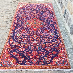 May include: A rectangular area rug featuring a deep purple background with an intricate floral pattern in shades of red, orange, light blue, and cream. The design includes a central medallion and a decorative border with white fringe at both ends.
