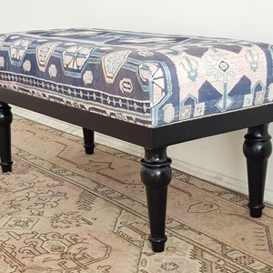 May include: A rectangular upholstered bench with a patterned fabric top in shades of blue, beige, and white. The bench has a black wooden frame and four turned black legs. The bench is a decorative furniture piece.